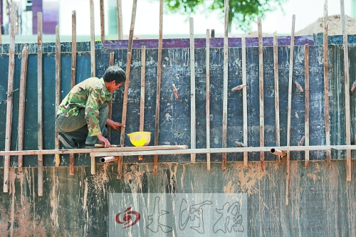 　　烈日下，狹窄的架子上，工人正用錘子固定樁基。