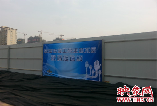 道路南側(cè)圍起了白色的圍擋，墻上標(biāo)示著“因地鐵施工帶來(lái)的不便敬請(qǐng)您諒解”的提示牌。