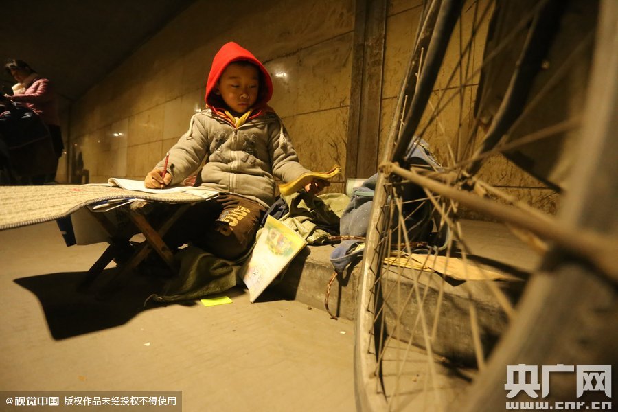 2015年11月8日晚，鄭州，7歲男孩涵洞橋下陪父母練攤，路邊燈下坐小馬扎上寫作業(yè)。