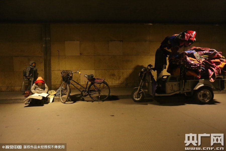 2015年11月8日晚，鄭州，7歲男孩涵洞橋下陪父母練攤，路邊燈下坐小馬扎上寫作業(yè)。