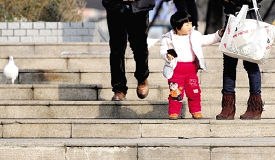 昨天中午，一女孩拉著家長(zhǎng)的手在紫荊山公園曬太陽(yáng)，氣溫升高，孩子的棉衣解開(kāi)了扣子。