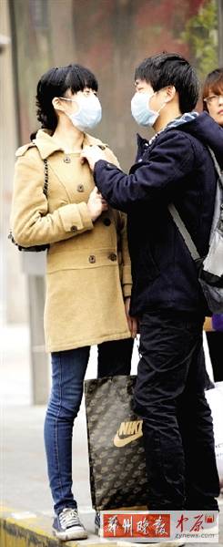 公交站臺(tái)上，一對(duì)年輕人戴著口罩，系緊衣領(lǐng)。